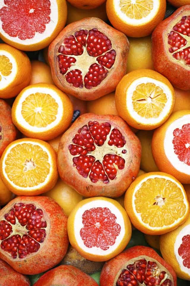 a mix of oranges and pomegranates sliced in half so their seeds show