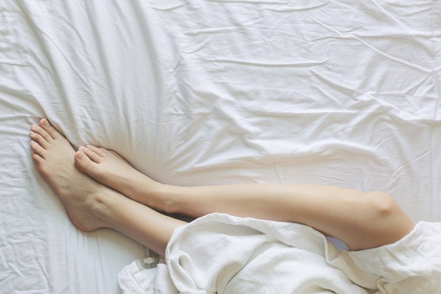 woman's feet laying in a bed with white sheets and bedding